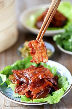 chopsticks holding meat on top of lettuce in a bowl with sauce