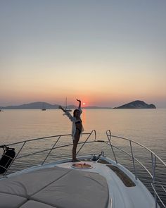 a woman standing on the back of a boat at sunset