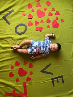 a baby laying on top of a green blanket covered in red and black paper hearts