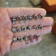 a person holding five different types of cross studs in their hand, each with an individual's name on it