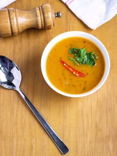 a white bowl filled with soup next to a wooden spoon and ladle on top of a table