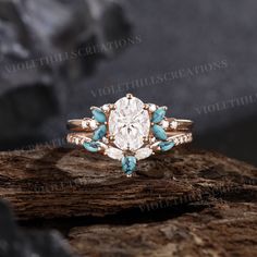 a white diamond ring with turquoise accents on top of a piece of wood and rocks