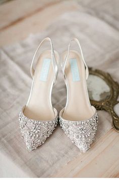 a pair of white high heeled shoes sitting on top of a wooden floor next to a mirror