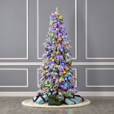 a brightly colored christmas tree with presents on the floor in front of a gray wall