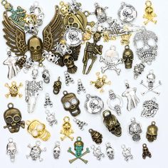 many different types and sizes of charms on a white surface, including skulls, crossbones, skull heads, and other metal objects