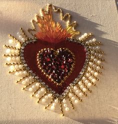 a heart shaped brooch with lots of pearls and beads on the side, sitting on a white table cloth