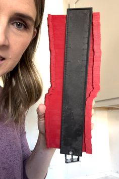 a woman holding up a piece of red and black paper in front of her face