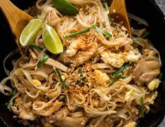 a plastic container filled with noodles and veggies next to a lime wedge on the side