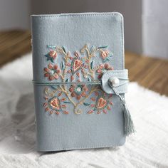 a small blue notebook with flowers and pearls on the front is sitting on a white blanket