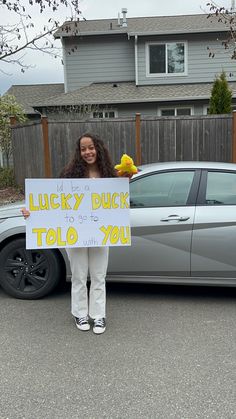 a woman standing in front of a car holding a sign that says lucky duck to go to you