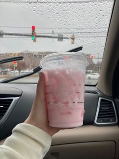 a person holding up a pink drink in their car