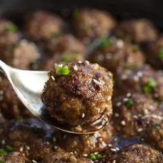 a ladle full of meatballs with sesame seeds and garnished with green onions