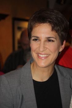 a woman with short hair smiling at the camera while wearing a gray jacket and black shirt