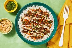 a blue plate topped with rice covered in meat and veggies next to two bowls