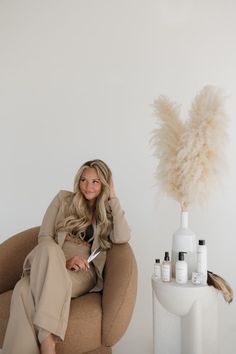 a woman sitting in a chair next to a vase with some hair on top of it