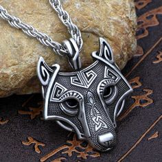 a necklace with a wolf head on it sitting next to a rock and some leaves