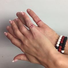 two hands with different colored bracelets holding each other's fingers and one has a small bow on it