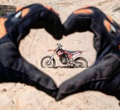 a dirt bike is in the shape of a heart with two hands holding it up