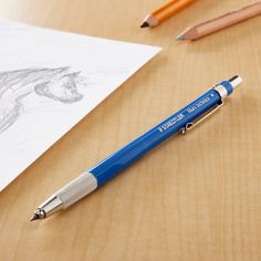 a blue pen sitting on top of a wooden table next to pencils and paper