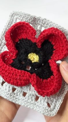 a crocheted red and black flower is being held by someone's hand