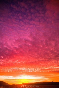 the sun is setting over some mountains and water with clouds in the sky above it