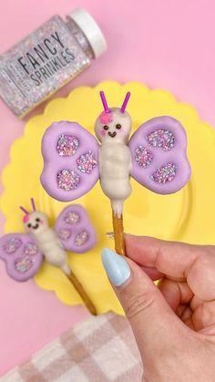 a person is holding some cake pops with butterfly decorations on them and there are other items in the background