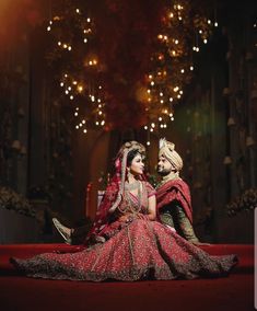 a bride and groom sitting on the floor in their wedding outfits with lights behind them