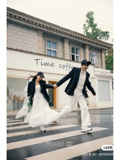 a man and woman walking across a cross walk holding hands in front of a building