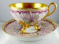 an ornate cup and saucer with gold trimmings on the rim, decorated with pink flowers