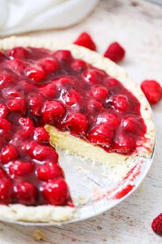 a cheesecake topped with raspberries on top of a white table next to some strawberries