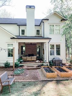 a white house with lots of plants in the front yard and patio area next to it