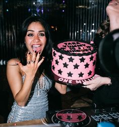 a woman holding a pink and black cake in front of her face with one hand