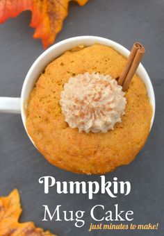 pumpkin mug cake with whipped cream in a white cup on a gray surface surrounded by autumn leaves