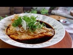 a white plate topped with meat and veggies covered in sauce on top of a wooden table