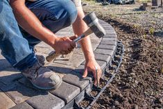 a man working on a brick walkway with a hammer