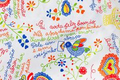 an embroidered fabric with colorful flowers and birds on it, which has words written in different languages