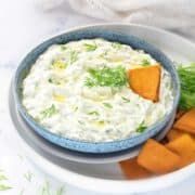 a bowl filled with dip surrounded by carrots and crackers on a white plate