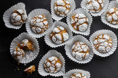 powdered sugar covered pastries in paper cups on a black surface with one bite taken out