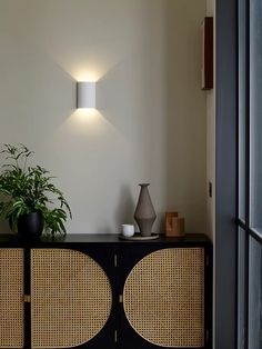 a wall light that is on the side of a cabinet next to a potted plant