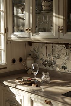 a kitchen counter with wine glasses on top of it and dishes in the cupboards