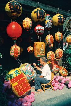 an old man sitting on a chair in front of some chinese lanterns and other decorations