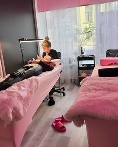 a woman sitting on a bed in a room with pink furniture and accessories around her