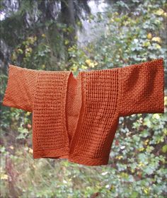 an orange knitted sweater hanging from a clothes line in front of trees and bushes