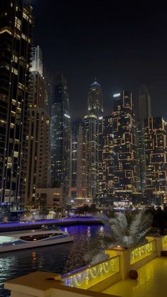 the city skyline is lit up at night with boats in the water and skyscrapers