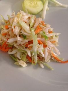 a white plate topped with coleslaw and cucumbers