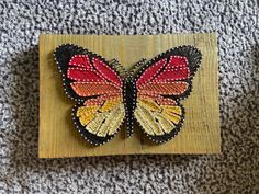 a butterfly is sitting on top of a piece of wood and beaded with beads