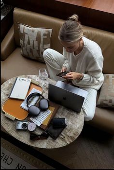 a woman sitting on a couch looking at her cell phone and laptop with headphones