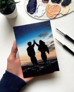 two people holding hands in front of some paintbrushes and other art supplies on a table