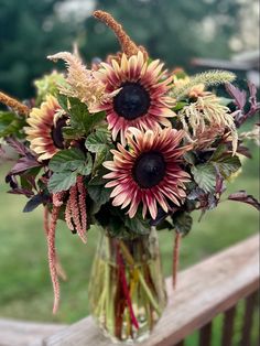 a vase filled with lots of flowers sitting on top of a wooden table next to a fence