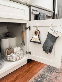 the kitchen cabinet is open and has gloves hanging from it's hooks on the door